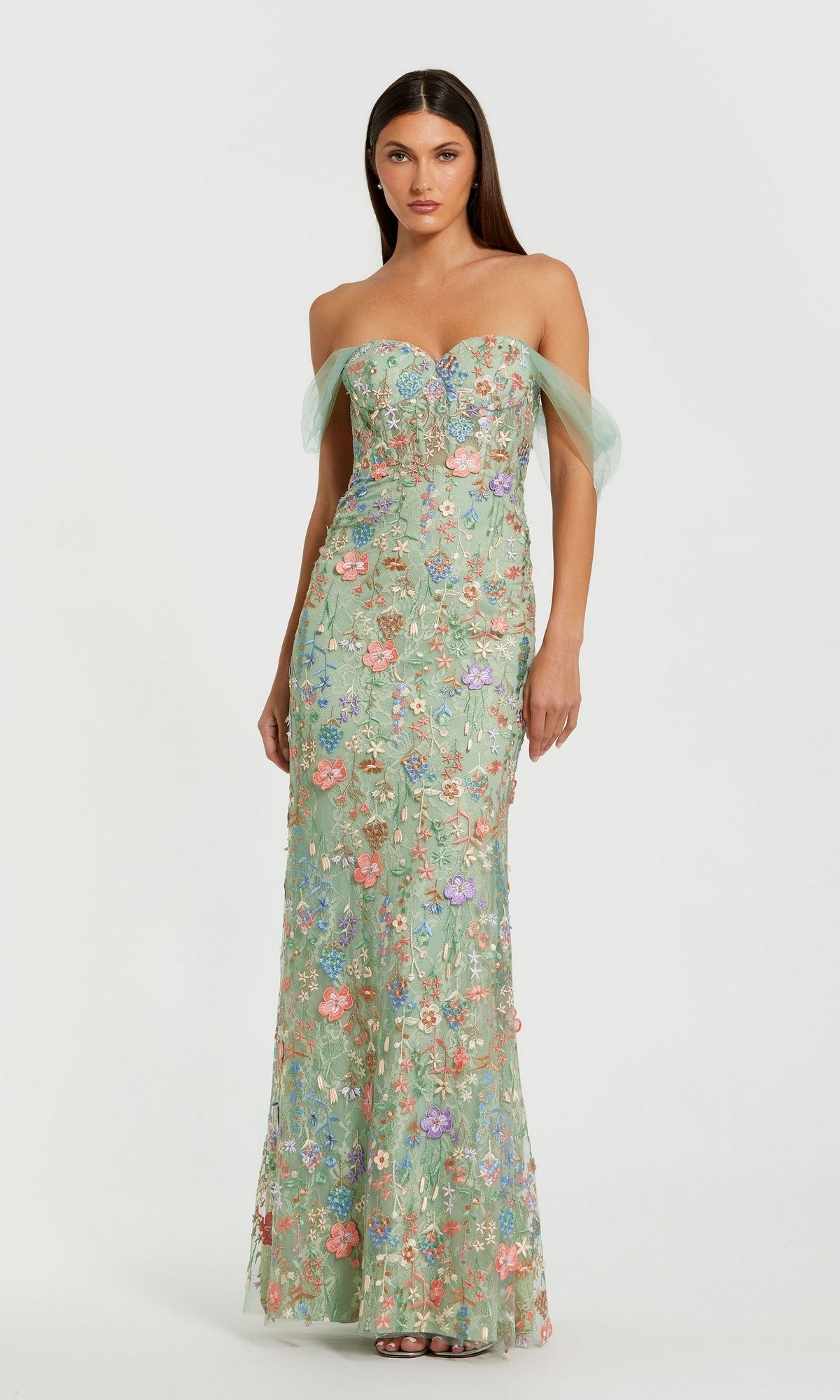 A woman stands against a plain background wearing the Mac Duggal 68809 Long Formal Dress in Sage Multi, featuring floral embroidery, a strapless fitted corset bodice, floor-length skirt, and sheer tulle off-the-shoulder sleeves.